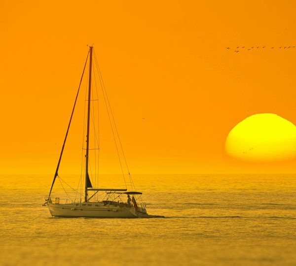 Un yate de lujo navegando suavemente al atardecer en el Estrecho de Gibraltar, con la costa de Tánger o el perfil de la Kasbah visible en la distancia y un cielo con colores cálidos. Disfrute de su navegación de lujo en Tánger.