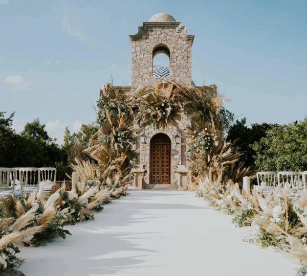 Una boda de lujo al aire libre, con una alfombra blanca que conduce a una capilla rústica adornada con plumas de pampa. Tu Boda de Lujo en Tánger.
